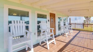 Un porche cubierto con sillas Adirondack blancas y una terraza de madera.