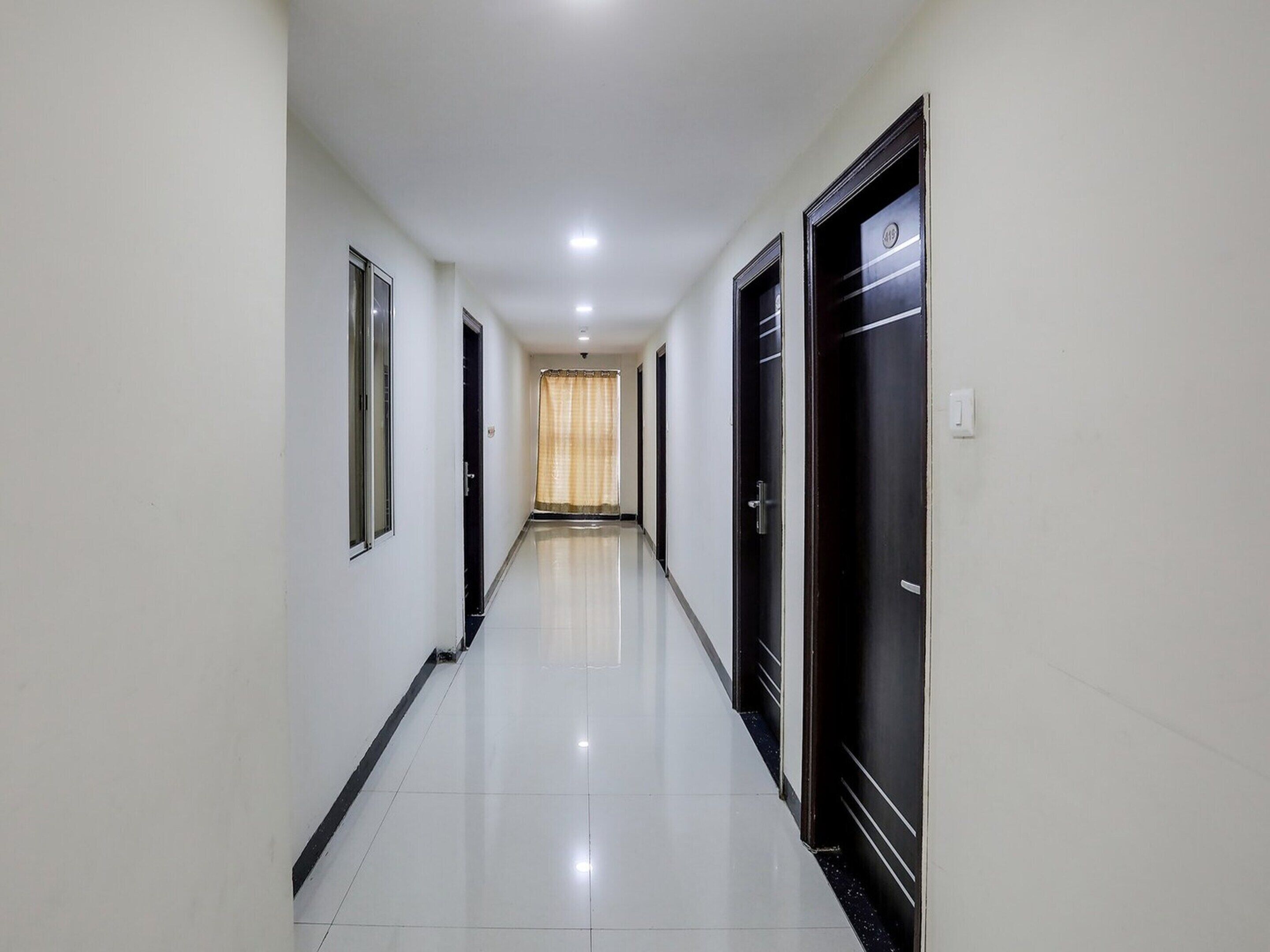 A long, narrow hallway with white walls and black doors, leading to a room with a curtain.