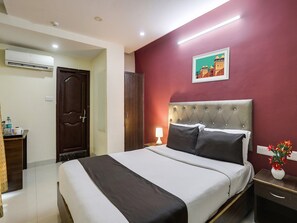 Een hotelkamer met een bed, nachtkastje, lamp, een foto aan de muur en een airconditioning.