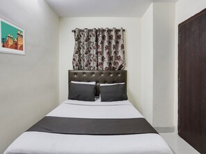 Un lit simple avec une tête de lit capitonnée, deux oreillers et une couvre-lit de couleur sombre.