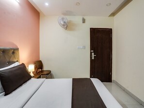 A hotel room with a bed, a chair, a desk, a desk lamp, a wall-mounted fan, and a door. - Super Collection O Lotus Grand (Hyderabad)