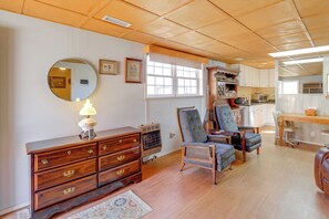 Ein Zimmer mit einem Holzkasten, zwei Sesseln, einem runden Spiegel und einem Fenster mit weißem Vorhang.