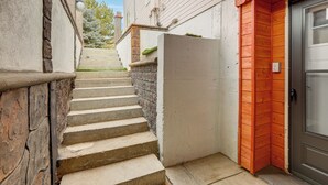 A narrow stairway leading to a door with a metal frame, adjacent to a white wall and a wooden fence. - Extended Stay in Denver! Cozy Apartment w/ Patio (Denver)