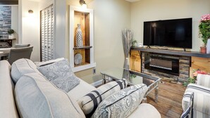 A modern living room with a sofa, a glass coffee table, a flat-screen TV, and a fireplace. - Extended Stay in Denver! Cozy Apartment w/ Patio (Denver)