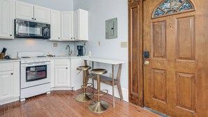 Una cucina con mobili bianchi, un forno a microonde, un forno e due sgabelli.