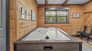 Une pièce avec une table de billard, des murs en bois, une fenêtre avec des rideaux et un tableau encadré accroché au mur.