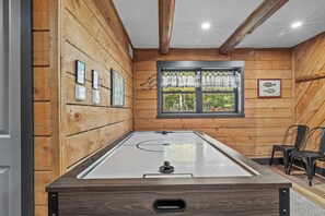 Ein Zimmer mit Billardtisch, Holzwänden, einem mit Vorhängen versehenen Fenster und einem gerahmten Bild an der Wand.