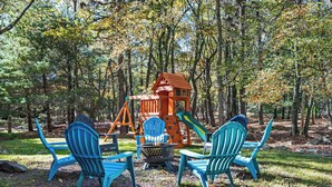Une aire de jeux avec un toboggan en bois et une structure d’escalade, le tout entouré d’arbres.