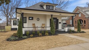 Une maison de plain-pied avec un porche à l’avant, un garage et un petit jardin devant la maison, agrémenté d’aménagements paysagers.
