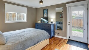 Ein Schlafzimmer mit Bett, Kommode, Fernseher und einer Tür zu einem Garten.