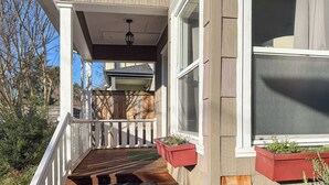 Eine Holzterrasse mit weißer Geländer, eine Holztreppe und zwei rote Pflanzkästen mit Pflanzen.