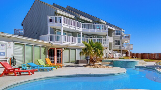 A multi-story building with a swimming pool, outdoor seating, and a palm tree. - Beach Boardwalk Stay, 10-Min Walk, 2-Min Drive (Port Aransas)