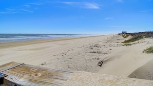 A beach with a wooden walkway leading to the shore, a sandy beach, and a distant building. - Beach Boardwalk Stay, 10-Min Walk, 2-Min Drive (Port Aransas)