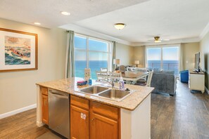 A modern kitchen with granite countertops and stainless steel appliances, a dining area with a view of the ocean, and a balcony with a view of the ocean. - Unwind Poolside, Walk to Shore! 12th-Floor PCB Gem (Panama City Beach)