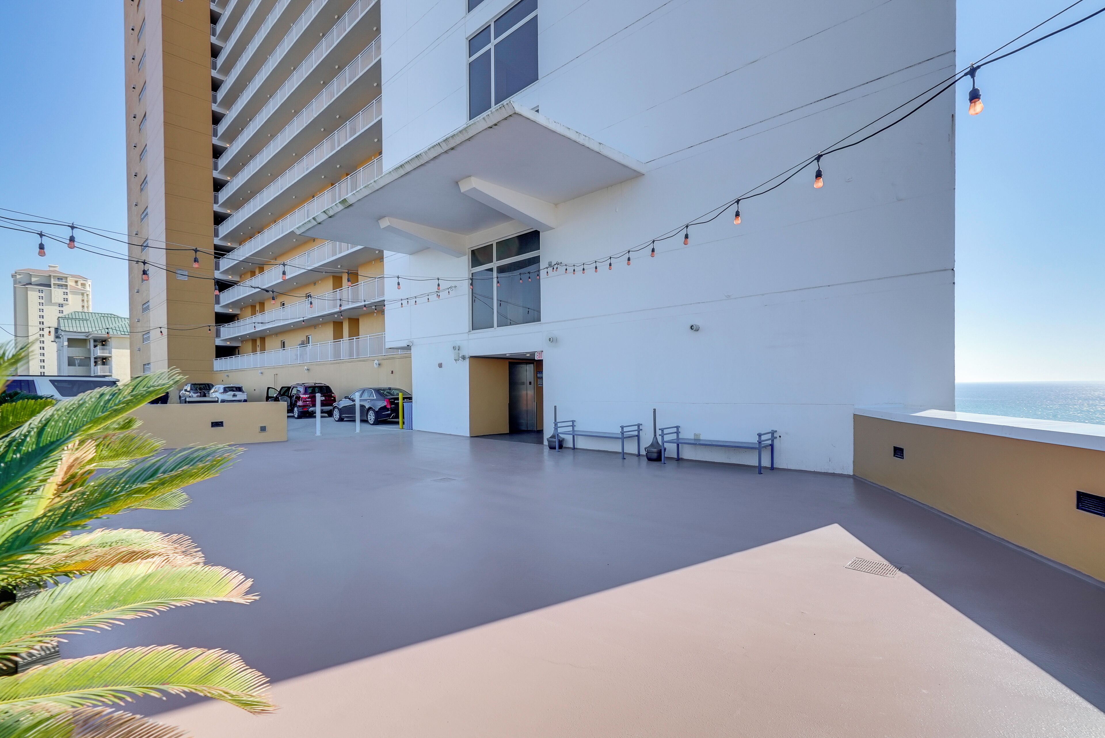 A rooftop terrace with a view of the ocean, featuring a building with multiple balconies and string lights.