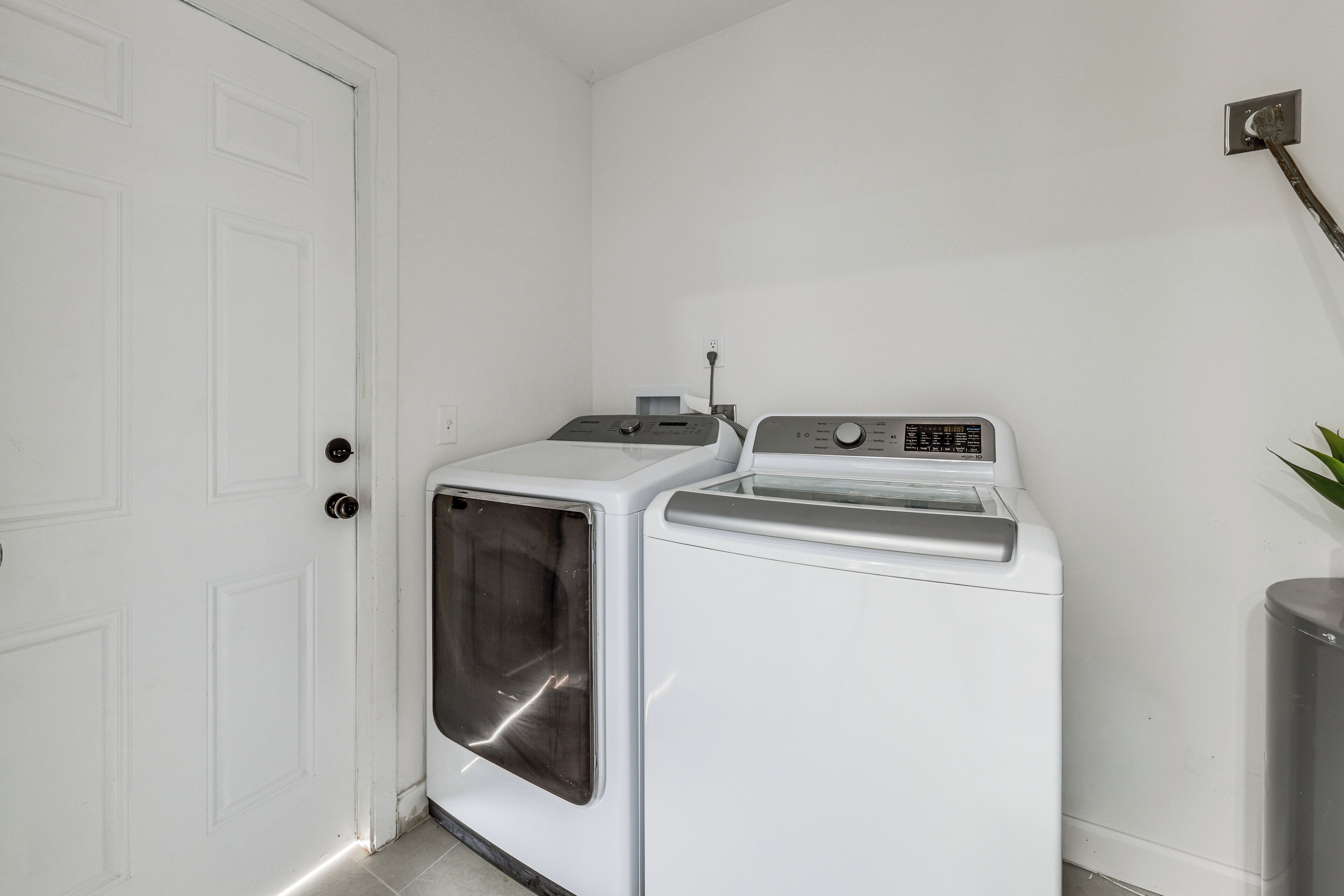 Een wasserette met een voorlader wasmachine en droger, een deur en een wandcontactdoos.