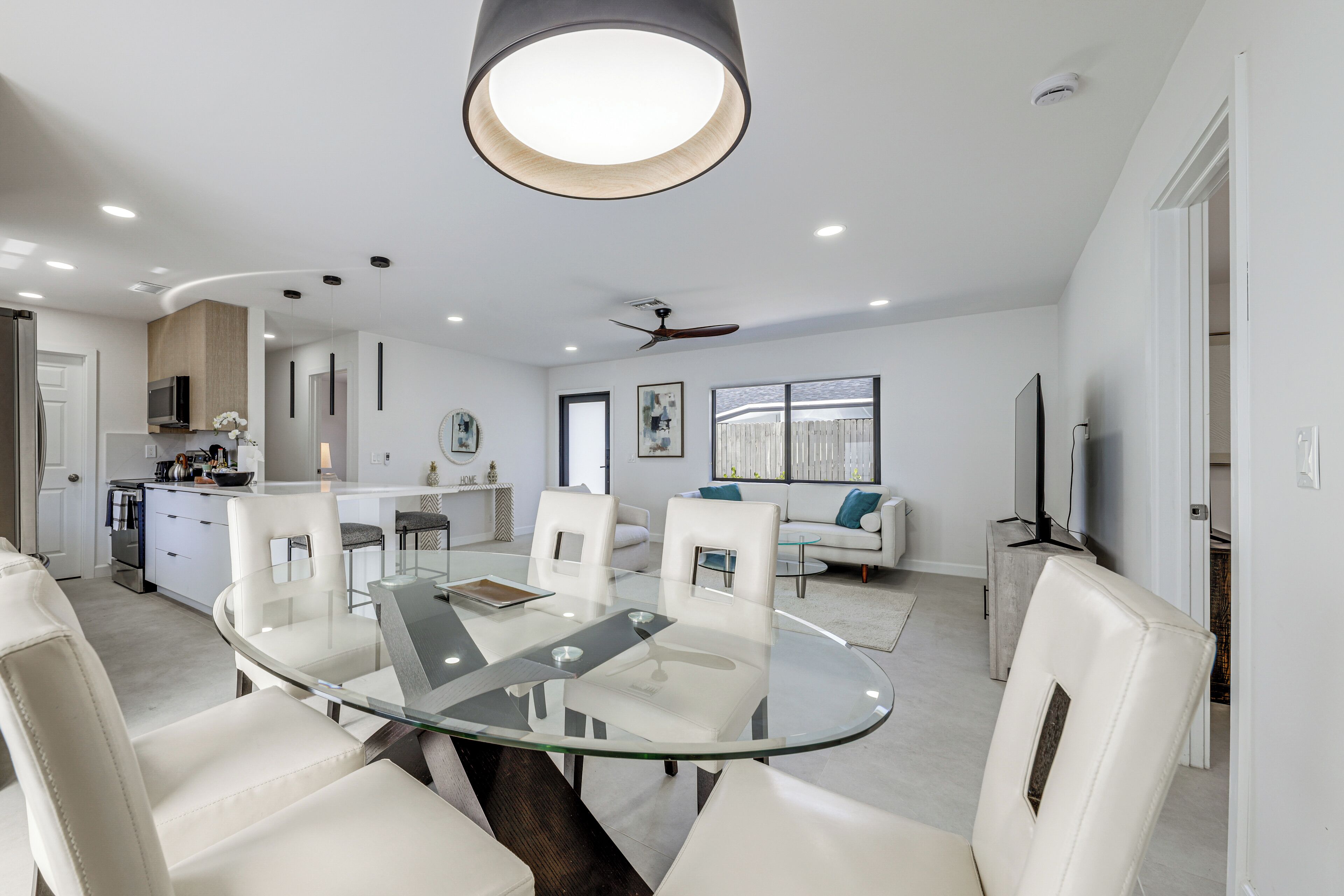 A modern kitchen with white cabinetry, a central island, and a dining area with a glass table and white chairs.