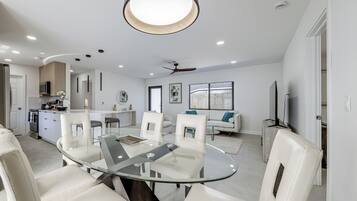 A modern kitchen with white cabinetry, a central island, and a dining area with a glass table and white chairs.