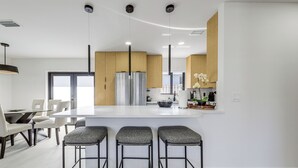 Eine moderne Küche mit einer zentralen Kochinsel, Barhocker und einem Essbereich mit Tisch und Stühlen.
