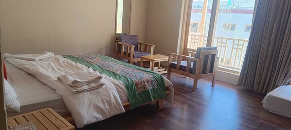 A room with a bed, two chairs, a small table, and a window with a view of the outside. - The Lha-Ri Nubra (Leh)