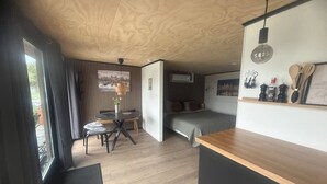 A compact room with a bed, a dining table with chairs, a small kitchen area, and a view through a window. - H2, Cozy B&B near Amsterdam - Free parking & Bikes (Lijnden)