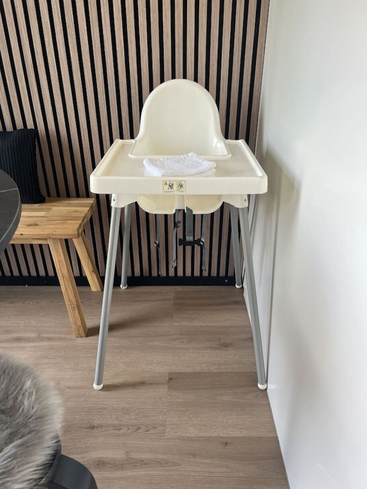 Una silla alta con bandeja, ubicada frente a un panel de madera con listones.