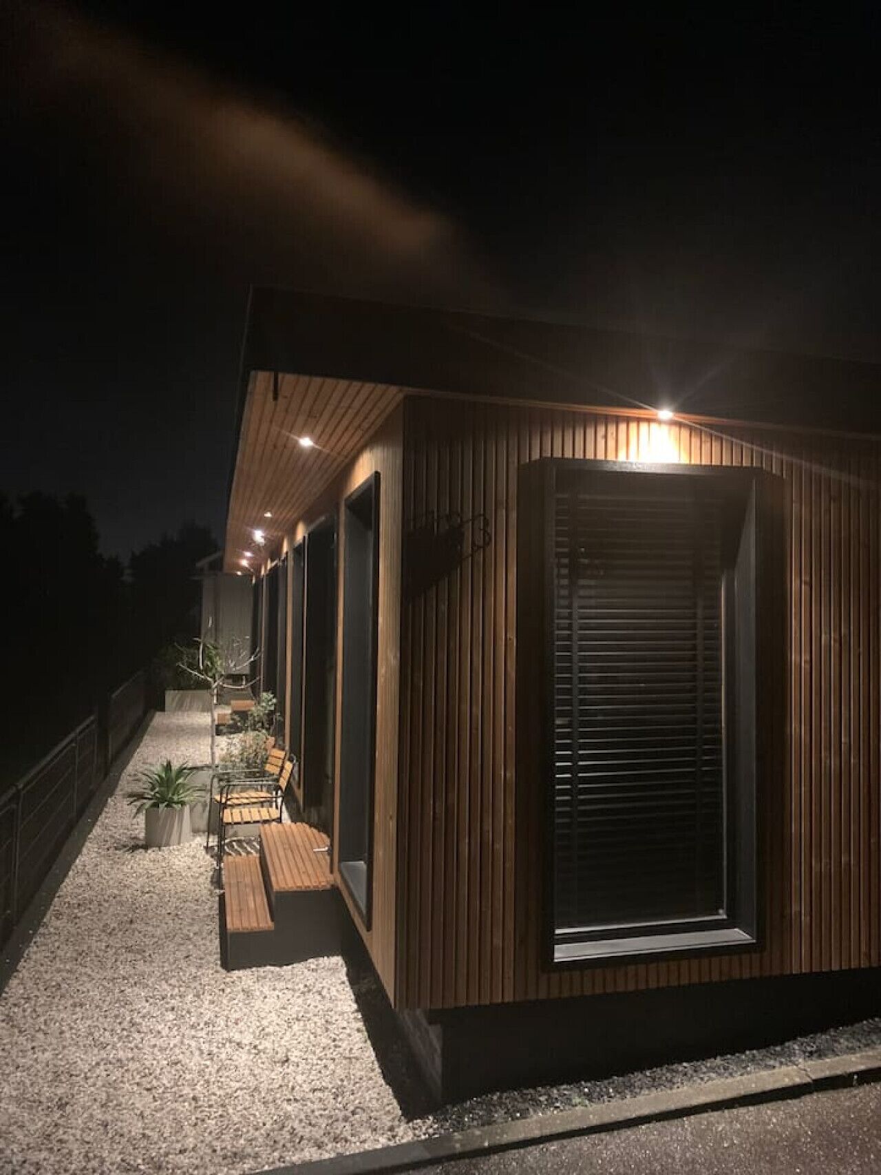 Een modern gebouw met een schuin dak, houten gevel en een overdekt terras met beplanting.