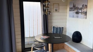 Ein Zimmer mit einem runden Tisch, zwei Stühlen, einer Bank, einem Gemälde und einem Fenster mit Vorhängen.
