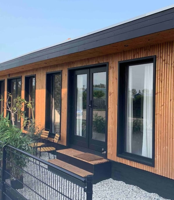 A modern building with large windows, a wooden exterior, and outdoor seating.