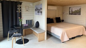 A cozy room with a bed, a desk with a chair, a small table with a vase of flowers, and a wall-mounted air conditioner.
