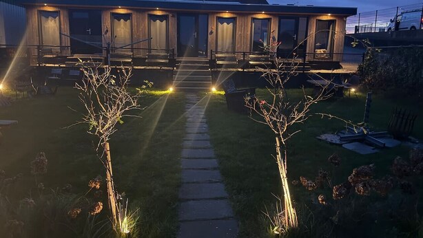 Ein modernes Gebäude mit gut beleuchtetem Eingang, einem Weg zum Eingang und einer kleinen Gartenanlage mit geschnittenen Büschen.