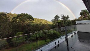 A glass balcony with a view of a forested hillside and a rainbow in the sky. - Spacious & Sunny House, Fantastic Bush Views, quiet and central location (East Killara)