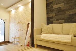 A modern living room with a brick wall, a sofa, and a hanging coat rack. - Entire 3BR Tennoji Home w/ Huge Balcony - Family-Friendly Osaka Retreat (大阪市阿倍野区美章園2丁目１２－７)
