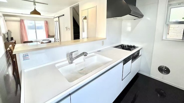 A modern kitchen with a white countertop, stainless steel sink, and black range hood.