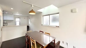 A modern kitchen with white cabinets, a dining area with a wooden table and chairs, and a large window with frosted glass.