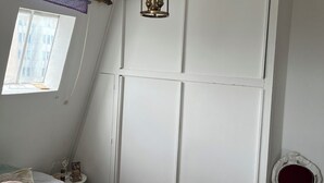 Una camera da letto con un letto, una finestra vista, un armadio bianco, una sedia rossa e una lampada a sospensione.