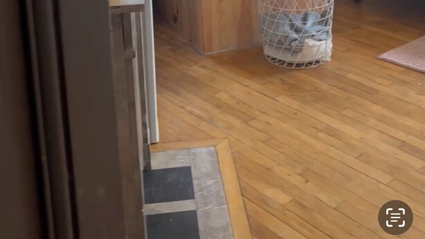 Una stanza con pavimento in legno, un letto con testiera bianca, un tavolino rotondo con un cesto e un angolo doccia con porta in vetro.