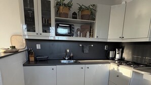A modern kitchen with white cabinets, a microwave, a sink, and a stove. There are potted plants on the countertop and a clock on the wall. - Holiday home for a family! (Katwijk aan Zee)