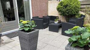 An outdoor patio with wicker furniture, potted plants, and a brick wall. - Holiday home for a family! (Katwijk aan Zee)
