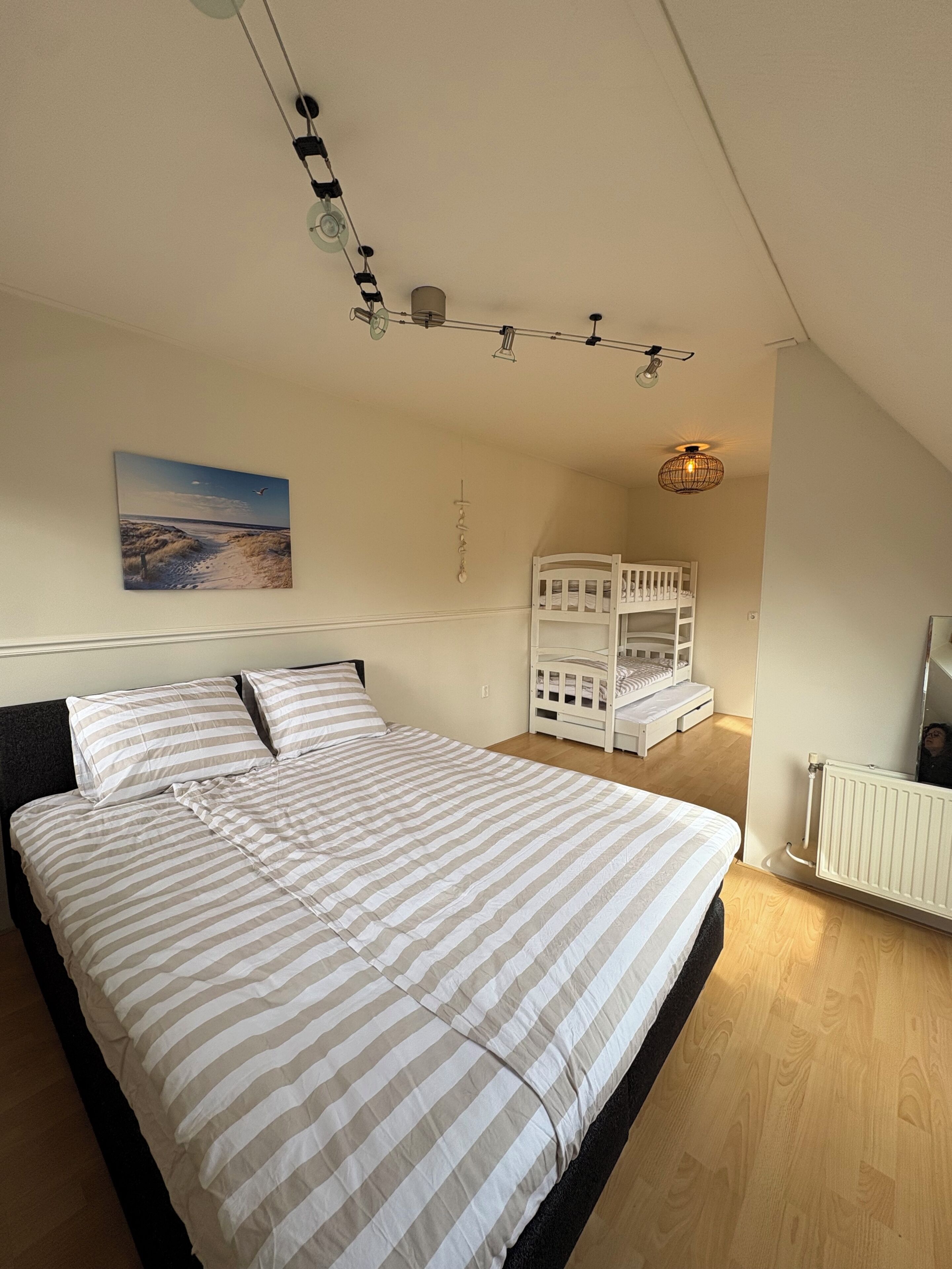 Ein Schlafzimmer mit einem Bett, Etagenbetten, einem Deckenventilator, einer Pendelleuchte, einem Gemälde und einer Heizung.
