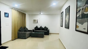 A spacious living area with a sofa set, a coffee table, and a wall-mounted air conditioner. - The Woods by Housiify  (Gurugram)