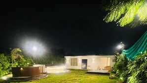 A well-lit outdoor area with a modern building, a stone pathway, and lush greenery. - The Woods by Housiify  (Gurugram)