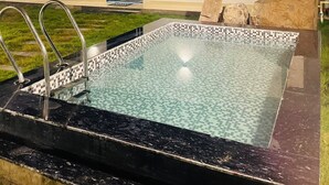 A rectangular outdoor swimming pool with a tiled edge, surrounded by a stone border. - The Woods by Housiify  (Gurugram)