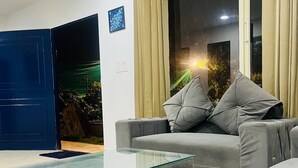 A modern living room with a grey sofa, a glass coffee table, and a large window with curtains. - The Woods by Housiify  (Gurugram)