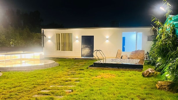 A modern house with a well-lit outdoor area, a pool, and a patio with seating. - The Woods by Housiify  (Gurugram)