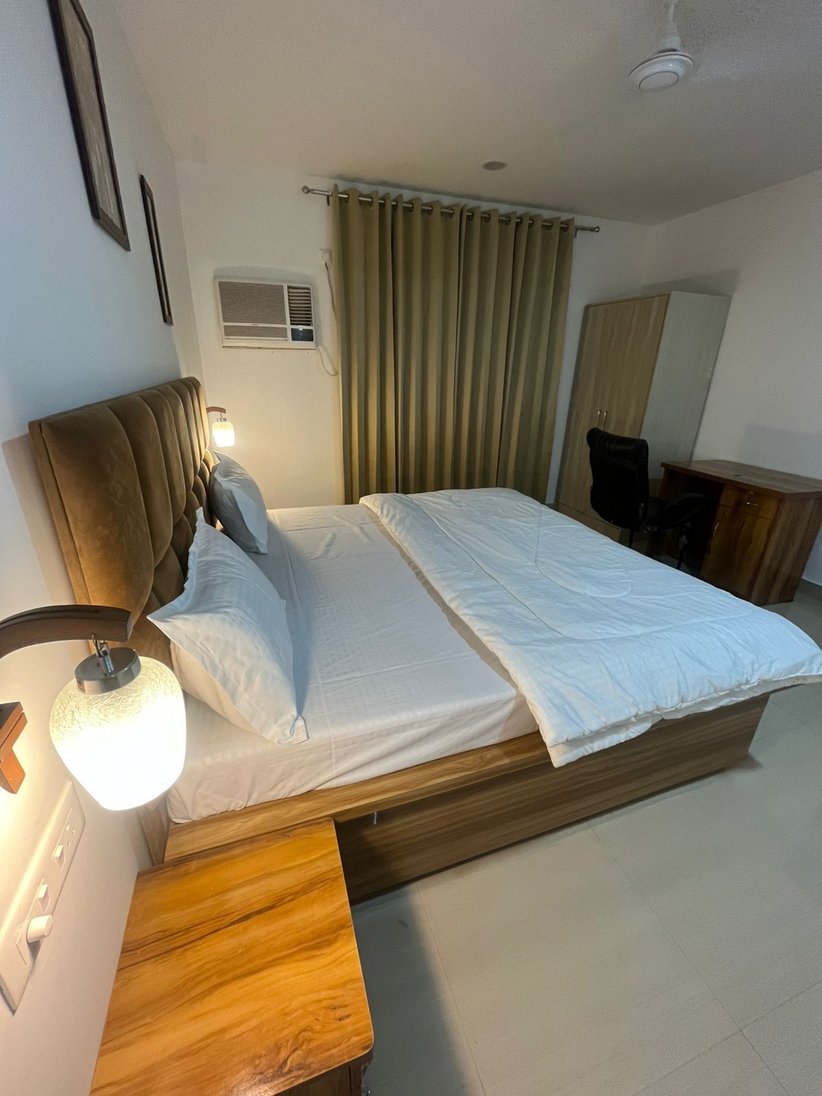 A hotel room with a wooden bed, a bedside lamp, a desk, and a mirror.