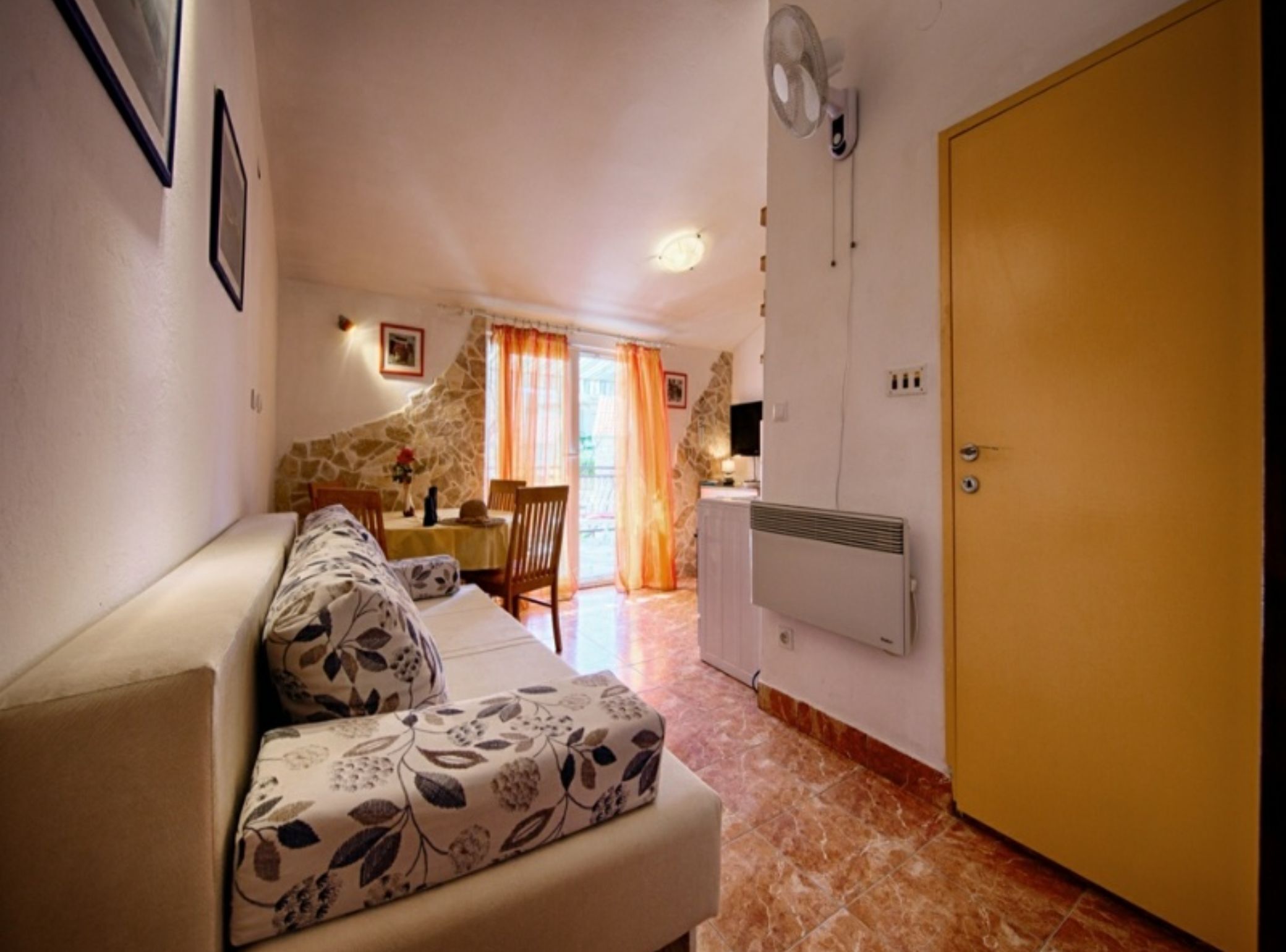 Una sala acogedora con un sofá, una mesa de comedor con sillas, una pared de piedra y una puerta.