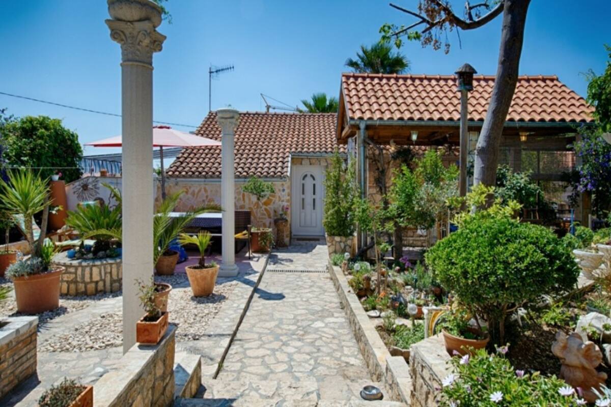 A courtyard with a stone pathway, potted plants, and a building with a tiled roof.