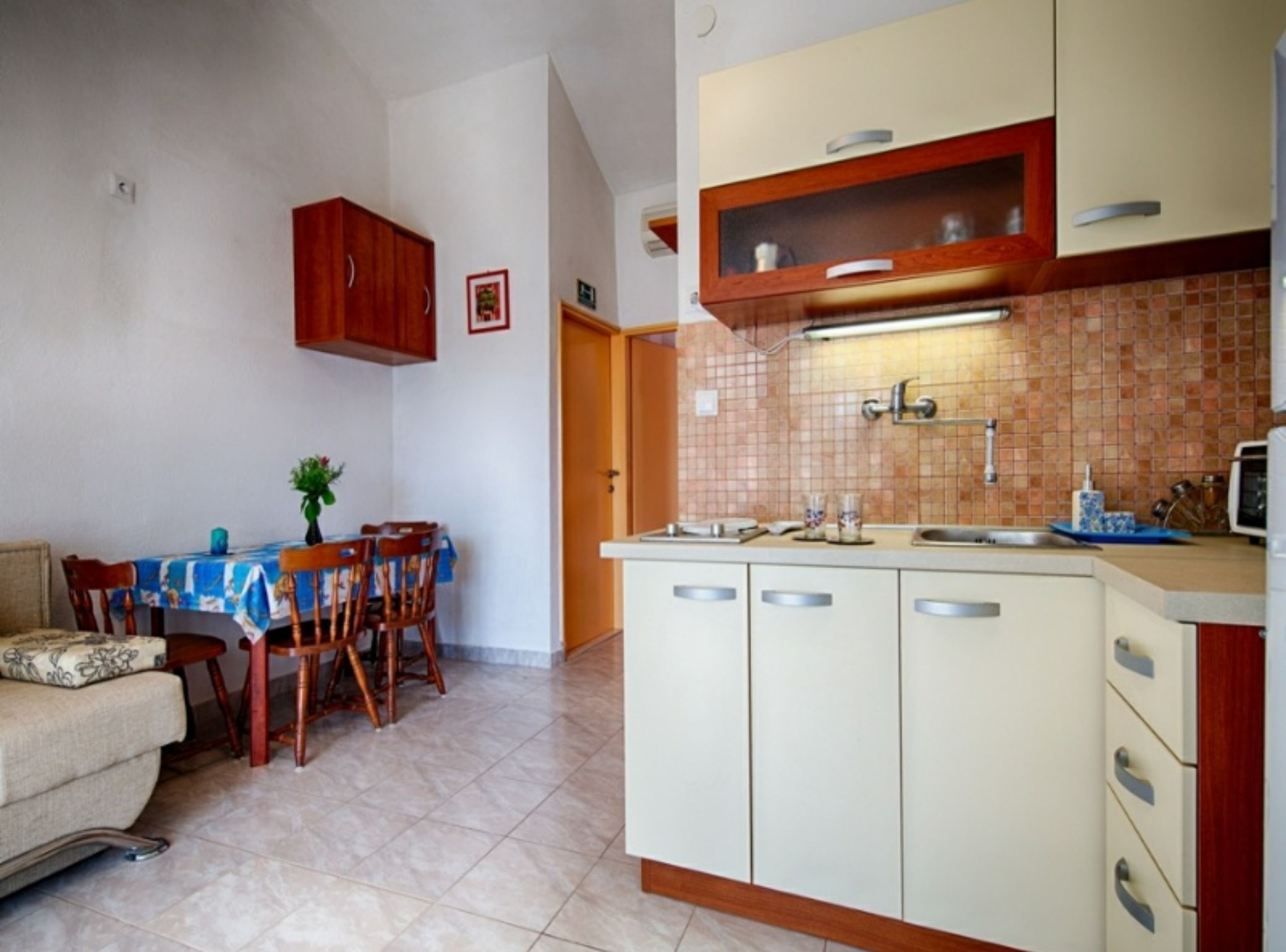 A compact kitchen with a dining area, featuring a tiled backsplash, wooden cabinets, and a tiled floor.