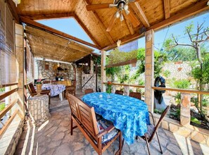 An outdoor patio with a table covered in a blue tablecloth, wooden chairs, and a ceiling fan. - Golden Coast Apartments (Vis)